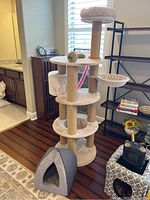 Multi-level beige cat tree with soft platforms and sisal-wrapped posts, next to gray soft pet bed.