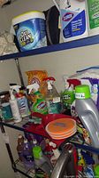 Photo showing shelves with OxiClean container, Clorox Clean-Up, and other assorted cleaning supplies including spray bottles and powder containers.