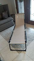 Side view of folding lounge chair with braided cream fabric and black frame, tag still attached
