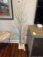 Front view of a white light up decorative tree showing the full height, branches, and base with electrical cord visible.