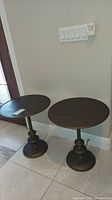 Two round metal side tables placed near a doorway on tiled floor showing overall condition and size.