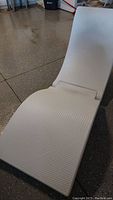 Close-up view of one white molded plastic pool lounge chair in a fully open position showing its textured surface with scratches.