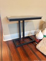 Side table placed on wooden floor next to wall with basket and cleaning supplies nearby