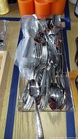 Clear overhead photo of the flatware set showing multiple spoons, forks, knives piled together in tray, highlighting hammered metal finish on handles.