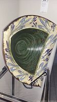 Triangular ceramic bowl with green swirl inside and beige/blue floral pattern on sides, displayed on a stand.
