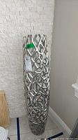 Photo of a tall slim silver metallic vase with an intricate open latticework design against a stone tile wall.