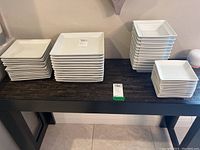 Overall view of stacks of white ceramic plates and bowls on a table.