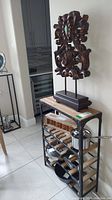 Photo showing the shelf with wine bottle slots and items on lower shelves, along with the large wood sculpture on top.
