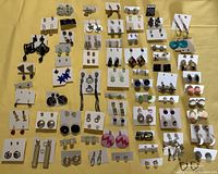 Photo of 100 pierced earrings with various colors and styles laid out on yellow cloth.