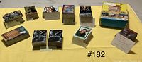 Wide shot of all eleven complete trading card sets displayed on yellow background including stacks and box set.
