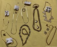 Photo showing assortment of necklaces, ring, earrings, brooch, and bracelets laid out on a yellow cloth background for identification and condition assessment.