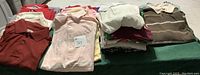 Folded stack of various men's shirts in assorted colors including reds, browns, and pastels.