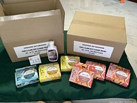 Photo showing two open cases containing multiple bottles of Paws & Claws premixed spot cleaner. Six boxed Youmop toilet sprays in different scent packaging are placed in front.