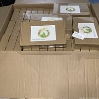 Open box with 43 sealed needle felting kits stacked inside, each kit is in a brown cardboard box with a label.