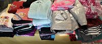 Photo showing folded assorted girls' clothes including a silver metallic gray coat on top, a pink tie-dye top, light blue fleece, and other assorted tops and bottoms.