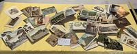 Wide view of a large group of assorted postcards scattered on a yellow surface, showing variety in size and imagery including buildings, nature, and people.