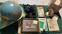 Photo of globe, binoculars, framed print, cross, book, styrofoam cutter, and beach bag showing lot items.
