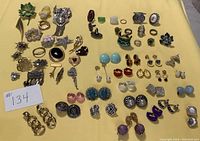 Full lot overview showing all earrings, pins/brooches, and rings on yellow background.