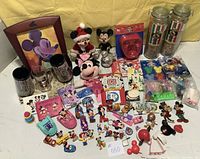 Photo showing entire assortment of Disney collectibles, including plush toys, jars of pasta, glassware, pins, and figures arranged on a white surface with yellow backdrop.