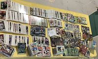 Large assorted stacks of football cards spread on a yellow tablecloth, showing a variety of players and teams from different decades