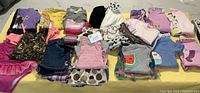 Photo showing full lot of toddler girls clothes laid out, including a peach bathing suit, various tops, bottoms, and a white fluffy jacket with poodle designs