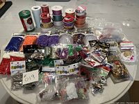 Photo of assorted craft ribbons, safety pins, beads in plastic bags, and various small craft decorations displayed on a table.