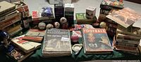 Photo showing a large collection of sports books, magazines, and several sports balls spread on a table.