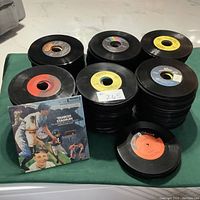 Multiple stacks of 45 RPM vinyl records with varied labels visible, some records with labels showing company logos and minor wear.