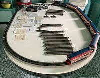 Complete train track assembled on table showing curved track forming an oval with papers laid out inside the track and train cars placed around outer edge.