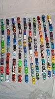 Top-down view of 100 diecast cars arranged in 10 rows of 10 on a white background showing the colorful variability and different models.