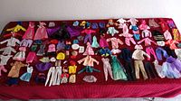 Full spread of over 100 Barbie and Ken clothes laid out on red surface