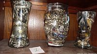 Three large glass jars filled with assorted vintage costume jewelry, including necklaces, rings, bracelets, and earrings, made of beads and gold/silver plated metals.