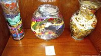 Three large jars filled with various colorful and gold/silver plated vintage costume jewelry pieces including beads, necklaces, bracelets, and rings.