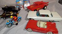 Group shot of all toy vehicles including black and red 57 Chevy models, Thunderbird, Low Rider Impala, Matchbox in packaging, and Western Germany police motorcycle toy