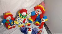 Photo showing 3 large plush clown dolls, clown face wall hanging on ground, and large red PEZ clown dispenser with blue hat