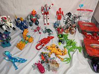 Wide shot showing the full assortment of action figures, plastic creatures, and Beyblade carrying cases.