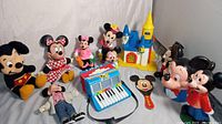 Overall view of vintage Disney lot including plush toys, plastic banks, playset castle, and musical accordion.