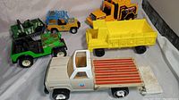 Photo showing the various vintage toy trucks including the Buddy L flatbed truck, green and yellow plastic jeeps, and yellow dump truck.