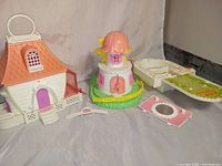Photo showing three CHARMKINS dollhouses and accessories arranged on a neutral background.