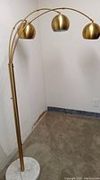Full view of vintage brass arc floor lamp with three golden spherical shades and white marble base in room corner.