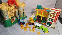 Full view of the vintage Fisher Price play family castle with stone facade and turrets, alongside the parking garage playset and several toy vehicles and road signs.