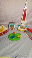 Photo showing vintage Fisher-Price toys including the Peek-A-Boo Screen TV, vacuum cleaner toy, playground toy, and musical record player box.