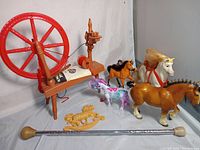 Photo showing vintage Remco Knitting Jenny wooden spinning wheel style knitting machine with red wheel, four plastic horse figurines of various sizes and colors, small wooden horse and chariot figurine, and a cheerleader twirling baton.