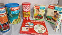 Full view of vintage toys lot including Tinkertoy cans, Playskool Village can, Lincoln Logs boxes, Spirograph box, and Fisher Price Village can.