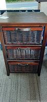 Front view of wood and wicker 3-drawer storage chest, drawers closed showing wicker fronts and leather-look handles.