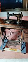 Full view showing the black decorated sewing machine mounted on a wooden cabinet with cast iron treadle base.