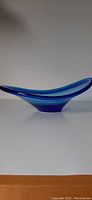 Side view of cobalt blue free-form glass bowl showing smooth, flowing organic shape and raised base.