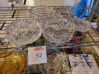 Five clear crystal pinwheel pattern ash trays on a metal shelf photographed from above.