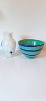 Front view of white glass vase with blue polka dots and lines next to turquoise blue bowl with blue stripes