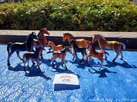 Group photo of all nine vintage Imperial Toy horse figurines on blue surface outdoors with greenery in background.